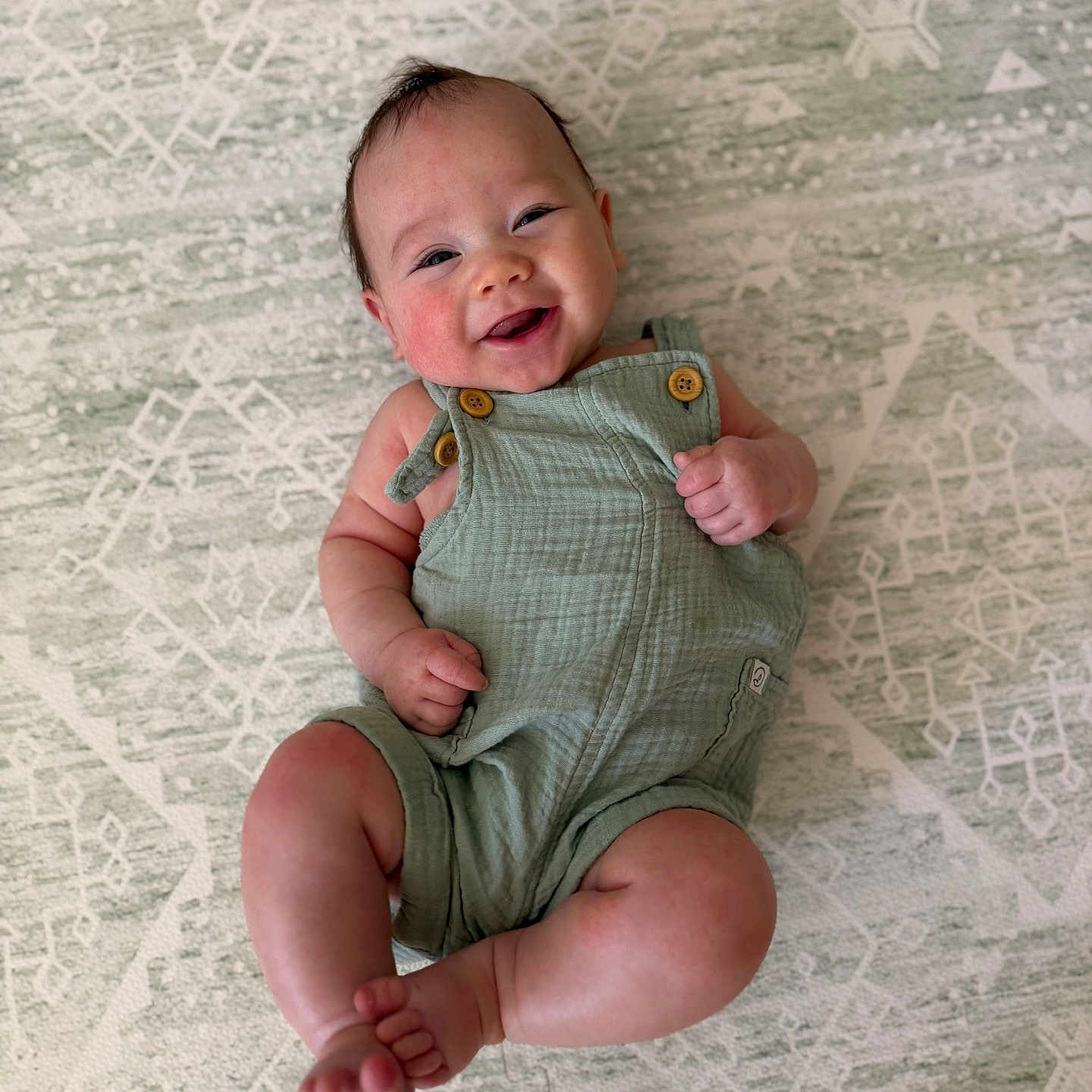 Easton joined the competition — help win amazing prizes! arms, baby, child, chubby_legs, comfort, cute, feet, green_romper, happy, head, indoors, infant, joy, lying_down, patterned_rug, portrait, skin, smiling, toes, wooden_buttons