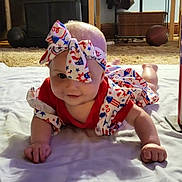 Naomi is registered to the contest to win money with this photo: baby, infant, tummy_time, patriotic_clothing, headband, blanket, carpet, living_room, fireworks, stars, stripes, red, white, blue, indoor, person, smiling, cute, celebration, floor