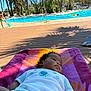 baby, towel, pool, water, child, palm_tree, outdoor, sunlight, shadow, deck, swimming, playing, summer, vacation, relaxation, clothing, people, blue_sky, nature, recreation