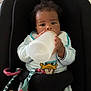baby, infant, bottle, feeding, baby_seat, curly_hair, striped_clothing, donald_duck, toy, indoor, child, cute, holding, drinking, seat_belt, black_seat, playful, young, portrait, comfort