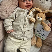 Tiago a rejoint le concours — aidez-le/la à gagner de superbes lots ! baby, child, smile, plush_toy, stuffed_animal, bear_pillow, bunny, sign, clothing, pants, shirt, hand, face, eyes, indoors, wood_floor, cute, infant, soft_toy, resting