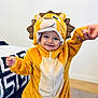 toddler, child, lion_costume, smiling, indoor, bedroom, hand_holding, plush, cute, yellow, brown, white, person, face, clothing, carpet, bed, happy, costume, young_child