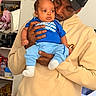 Philip is registered to the contest to win money with this photo: baby, child, man, holding, hoodie, blue_clothing, indoor, shelf, affection, casual, portrait, person, expression, clothing, hand, face, headwear, hat, skin, room