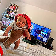 Philip joined the competition — help win amazing prizes! baby, child, person, hand, tattoo, bed, bedroom, cap, red_cap, clothing, furniture, television, shelf, indoor, casual, expression, cute, holding, smiling, home