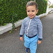 Alex a rejoint le concours — aidez-le/la à gagner de superbes lots ! child, toddler, boy, hoodie, blue_pants, sneakers, sidewalk, hedge, greenery, outdoor, smiling, walking, casual_clothing, daylight, nature, young_child, person, street, urban, happy
