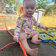 Kaylee-Anah joined the competition — help win amazing prizes! baby, barefoot, blue_eyes, child, concrete, curious, daytime, fence, garden, hair_tie, outdoor, person, plastic, play, sitting, summer, sunny, swimsuit, toy, water_toy