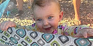 Kaylee-Anah joined the competition — help win amazing prizes! baby, blue_eyes, child, clothing, colorful, cute, face, feet, ground, hands, happy, mesh, outdoor, patterned_fabric, pigtails, playpen, shadow, smiling, sunlight, toys