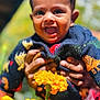 baby, child, smiling, happy, face, hands, flower, marigold, yellow_flower, outdoor, nature, colorful_clothing, sweater, animal_pattern, portrait, closeup, sunlight, joy, person, cute