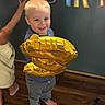 Tristan is registered to the contest to win money with this photo: toddler, child, birthday, balloon, golden_balloon, smiling, happy, standing, barefoot, indoor, party, celebration, birthday_letters, wooden_floor, portrait, blond_hair, blue_shirt, gray_pants, playful, family