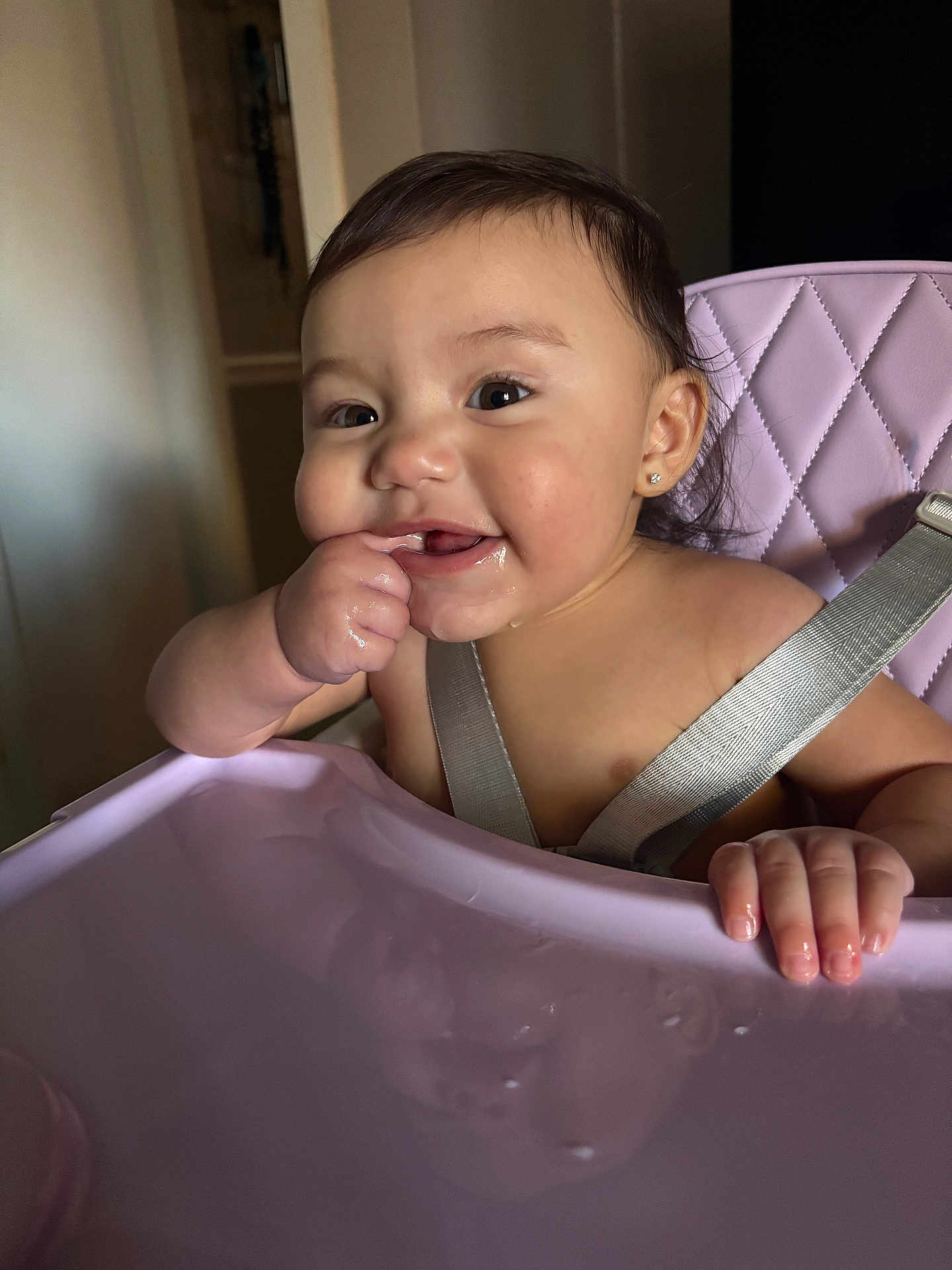 Jasliani is registered to the contest to win money with this photo: baby, high_chair, child, smiling, finger_in_mouth, harness, indoor, happy, cute, person, face, skin, earring, hair, reflection, table, seat, infant, toddler, domestic