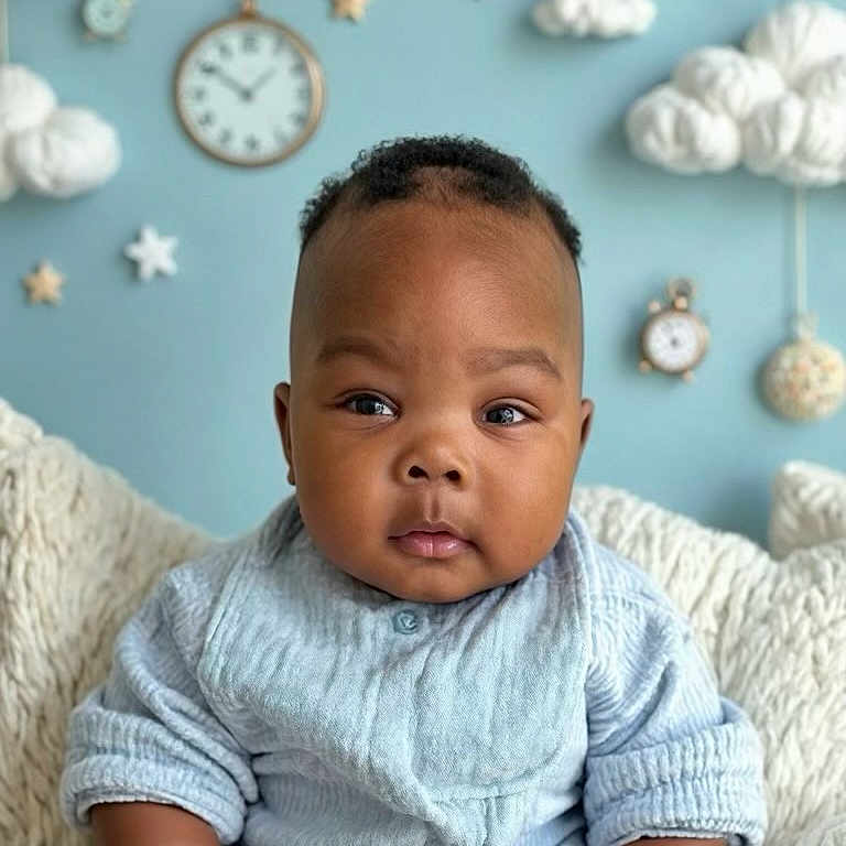 Abdoul Kiyaan joined the competition — help win amazing prizes! baby, blanket, blue_clothing, child, clock, closeup, clouds, curious, cute, expression, face, fluffy, head, indoor, infant, nursery, portrait, seated, soft_lighting, stars