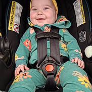Zoey is registered to the contest to win money with this photo: baby, child, car_seat, smiling, headband, yellow, green, floral, clothing, straps, safety, happy, infant, cute, portrait, seat, baby_clothes, indoor, child_seat, closeup