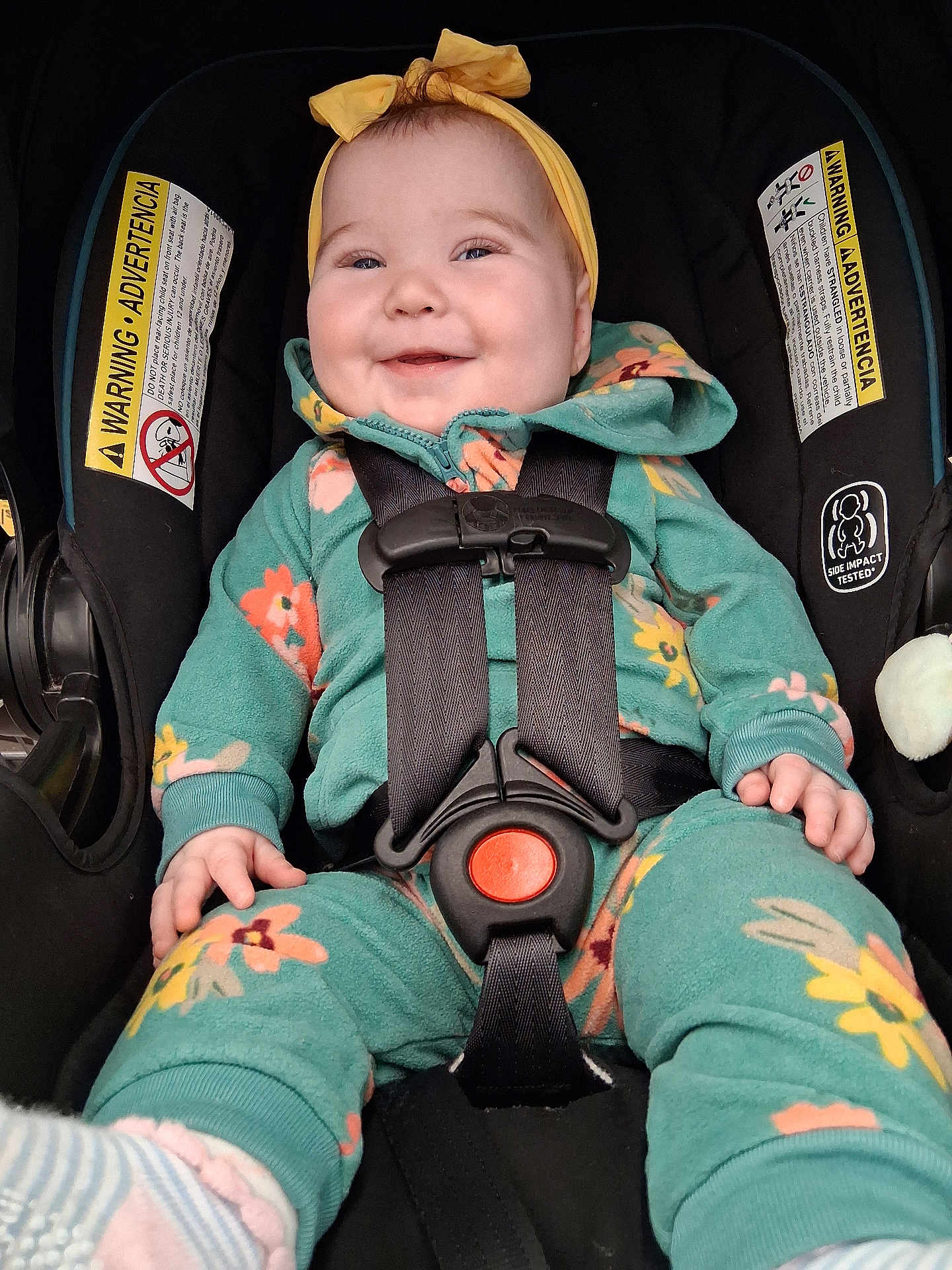 Zoey is registered to the contest to win money with this photo: baby, child, car_seat, smiling, headband, yellow, green, floral, clothing, straps, safety, happy, infant, cute, portrait, seat, baby_clothes, indoor, child_seat, closeup