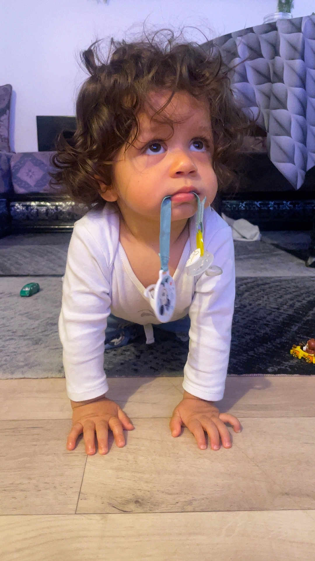 Mylhan a rejoint le concours — aidez-le/la à gagner de superbes lots ! toddler, child, baby, curly_hair, pacifier, crawling, floor, indoor, living_room, carpet, toy, white_clothing, hands, face, expression, looking_up, cute, young_child, home, curiosity