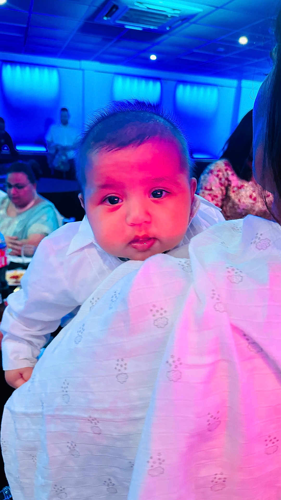Taaj joined the competition — help win amazing prizes! baby, child, infant, person, face, portrait, clothing, white_shirt, blanket, holding, indoor, people, adult, seated, table, food, drink, lighting, blue_light, pink_light
