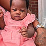 Princess is registered to the contest to win money with this photo: baby, infant, pink_dress, clothing, person, arm, hand, tattoo, watch, bracelet, skin, face, expressionless, closeup, outdoor, brick_wall, fabric, sitting, holding, adult