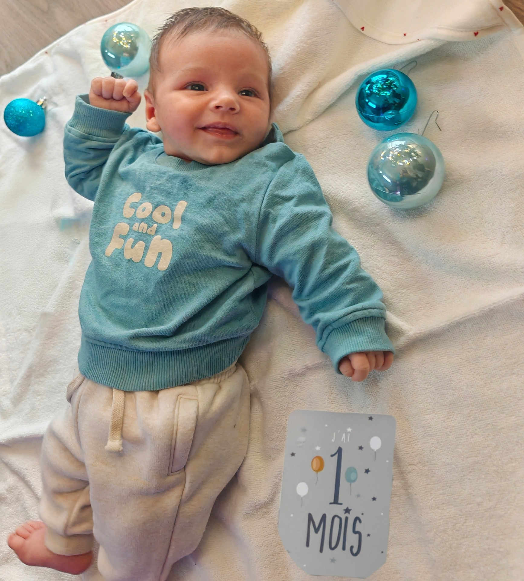 Jules participe au concours pour gagner de l'argent avec cette photo : baby, smile, blue_sweatshirt, milestone_card, blanket, christmas_ornaments, white_blanket, infant, cute, happy, clothing, person, indoors, one_month, baby_girl_or_boy, cute_expression, soft_lighting, small_hands, pale_pants, lying_down