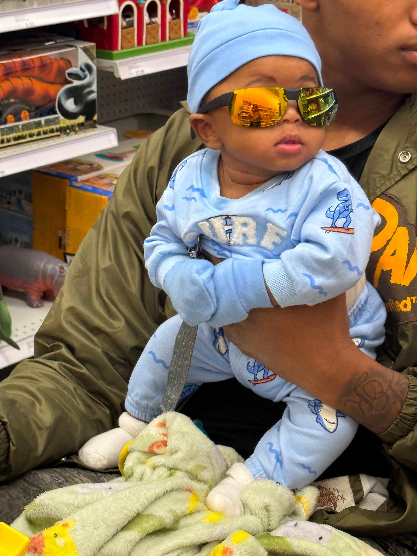 Navy joined the competition — help win amazing prizes! baby, child, sunglasses, blue_clothing, dinosaur_print, blanket, adult_hand, toy_store, shelf, person, holding, cute, indoor, reflection, jacket, casual_wear, infant, fashion, accessory, portrait