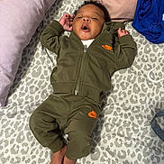 Navy is registered to the contest to win money with this photo: baby, infant, child, person, bed, blanket, pillow, clothing, tracksuit, nike, foot, face, hair, pattern, fabric, relaxed, indoors, laying_down, cute, sleepwear