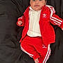Zavannah is registered to the contest to win money with this photo: baby, infant, red_tracksuit, adidas, clothing, bed, black_bedspread, floor, plaid_pants, person, footwear, indoor, portrait, smiling, cute, child, lying_down, looking_at_camera, young, casual_wear