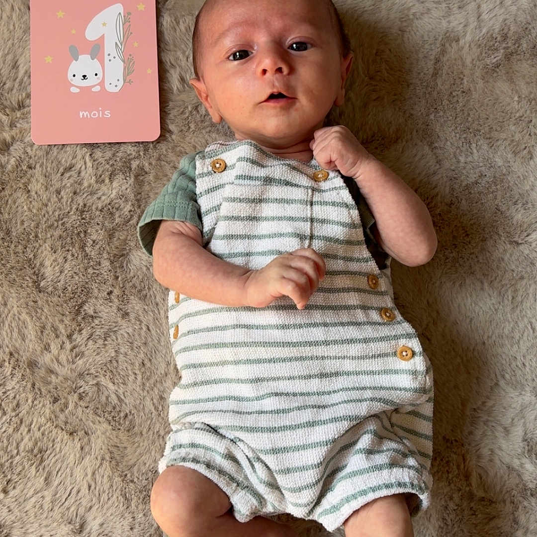 Adrio participe au concours pour gagner de l'argent avec cette photo : baby, blanket, bunny_illustration, curious_expression, cute, face, foot, green_shirt, hand, indoors, infant, lying_down, milestone_card, month_marker, newborn, pink_card, portrait, romper, soft_texture, striped_clothing
