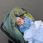 Izak a rejoint le concours — aidez-le/la à gagner de superbes lots ! baby, infant, pacifier, car_seat, stroller, blanket, hat, canopy, pavement, outdoor, safety_label, buckle, handle, face, eyes, hood, blue_clothing, white_blanket, muslin, newborn