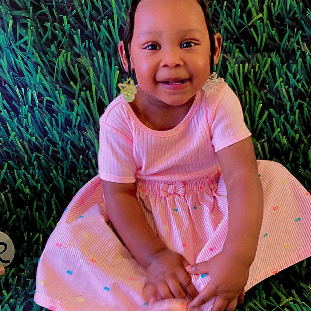 Giavonni joined the competition — help win amazing prizes! background, barefoot, child, colorful, cute, earrings, fashion, grass_pattern, hair_up, happy, indoor, person, pink_dress, playful, portrait, sitting, smiling, studio, toddler, young_child