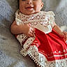 baby, smiling, red_dress, headband, flower, lace, blanket, lying_down, infant, cute, happy, child, portrait, soft_texture, indoors, young, person, skin, hand, foot
