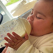 Dulcé a rejoint le concours — aidez-le/la à gagner de superbes lots ! baby, bottle, milk, feeding, sleepy, child, hand, clothing, indoor, window, daylight, plastic_chair, greenery, face, person, cozy, cute, infant, portrait, relaxed