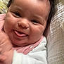 baby, infant, smiling, face, tongue_out, close_up, blanket, pink_bib, white_clothing, happy, cute, chubby_cheeks, dark_hair, indoors, soft_texture, portrait, child, person, newborn, playful