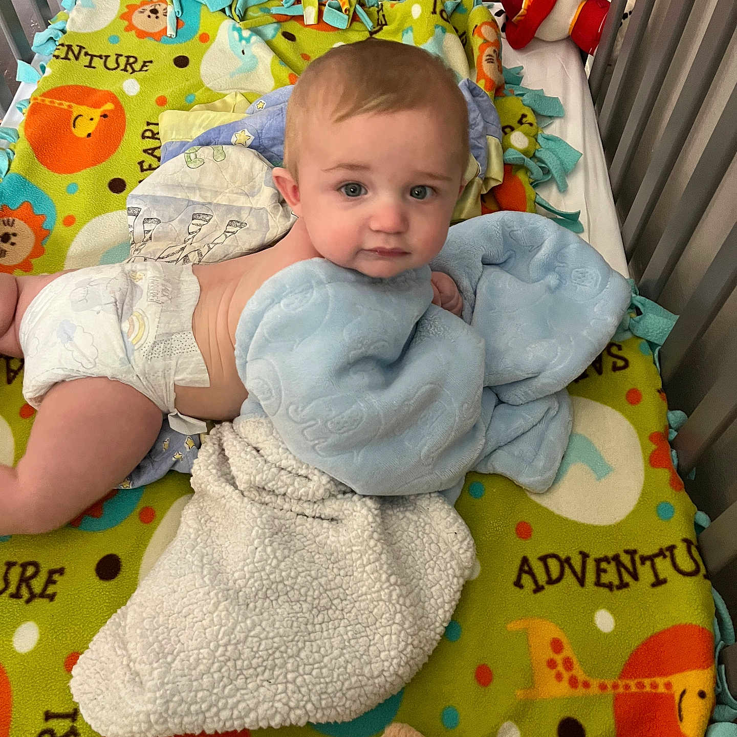 Malakai is registered to the contest to win money with this photo: baby, bedroom, blanket, blue_eyes, child, colorful, comfort, crib, cute, diaper, face, head, indoor, infant, laying_down, nursery, plush_toy, safari_pattern, soft_toy, toddler