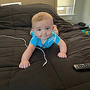 Malakai is registered to the contest to win money with this photo: baby, blue_clothing, bed, black_bedspread, charging_cable, child, curious, daylight, face, furniture, indoor, lying_down, person, remote_control, room, window, window_blinds, young_child, hands, head
