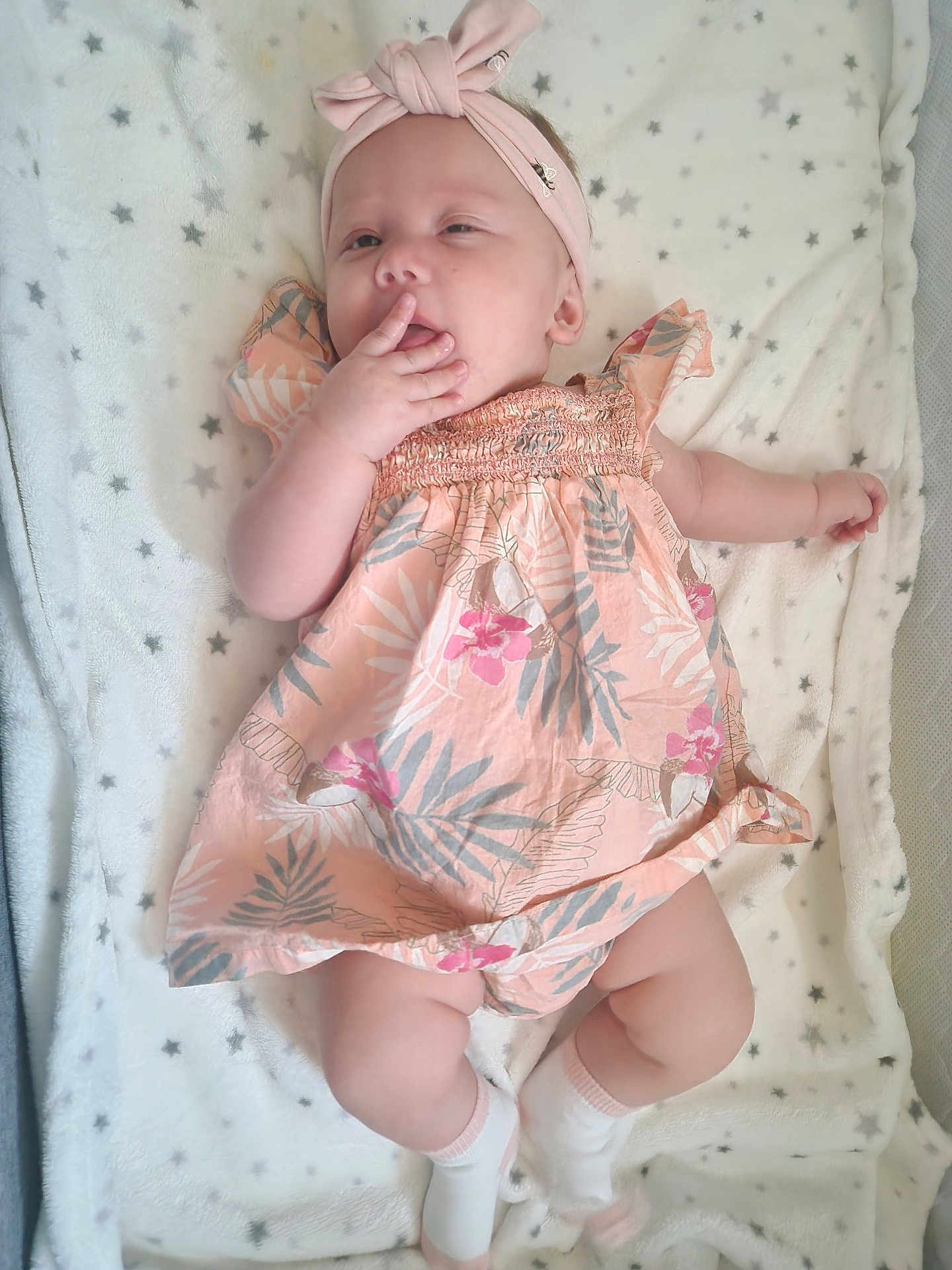 Lennox Arizona is registered to the contest to win money with this photo: baby, infant, child, dress, headband, blanket, star_pattern, socks, lying_down, hand, face, skin, cute, sleepy, soft_texture, pink, white, floral, comfort, relaxed
