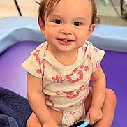 Mia is registered to the contest to win money with this photo: toddler, child, smiling, hair_bows, toothbrush, sitting, purple_mat, blanket, indoor, cute, happy, person, baby, clothing, playtime, face, skin, head, expression, young_child