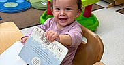 Mia joined the competition — help win amazing prizes! book, child, clothing, daycare, flooring, hair, happy, high_chair, indoor, nursery, person, play_area, playtime, reading, seat, smile, table, toddler, toy, wooden_furniture