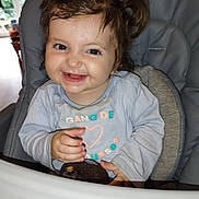 Léanna a rejoint le concours — aidez-le/la à gagner de superbes lots ! toddler, child, smile, happy, high_chair, avocado, curly_hair, pigtails, indoor, window, natural_light, baby_clothing, face, person, cute, playful, food, furniture, portrait, infant