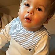 Even a rejoint le concours — aidez-le/la à gagner de superbes lots ! toddler, child, face, portrait, indoor, clothing, bib, white_outfit, curious_expression, seated, young_child, baby, light_skin, blond_hair, warm_lighting, person, cute, closeup, infant, soft_texture