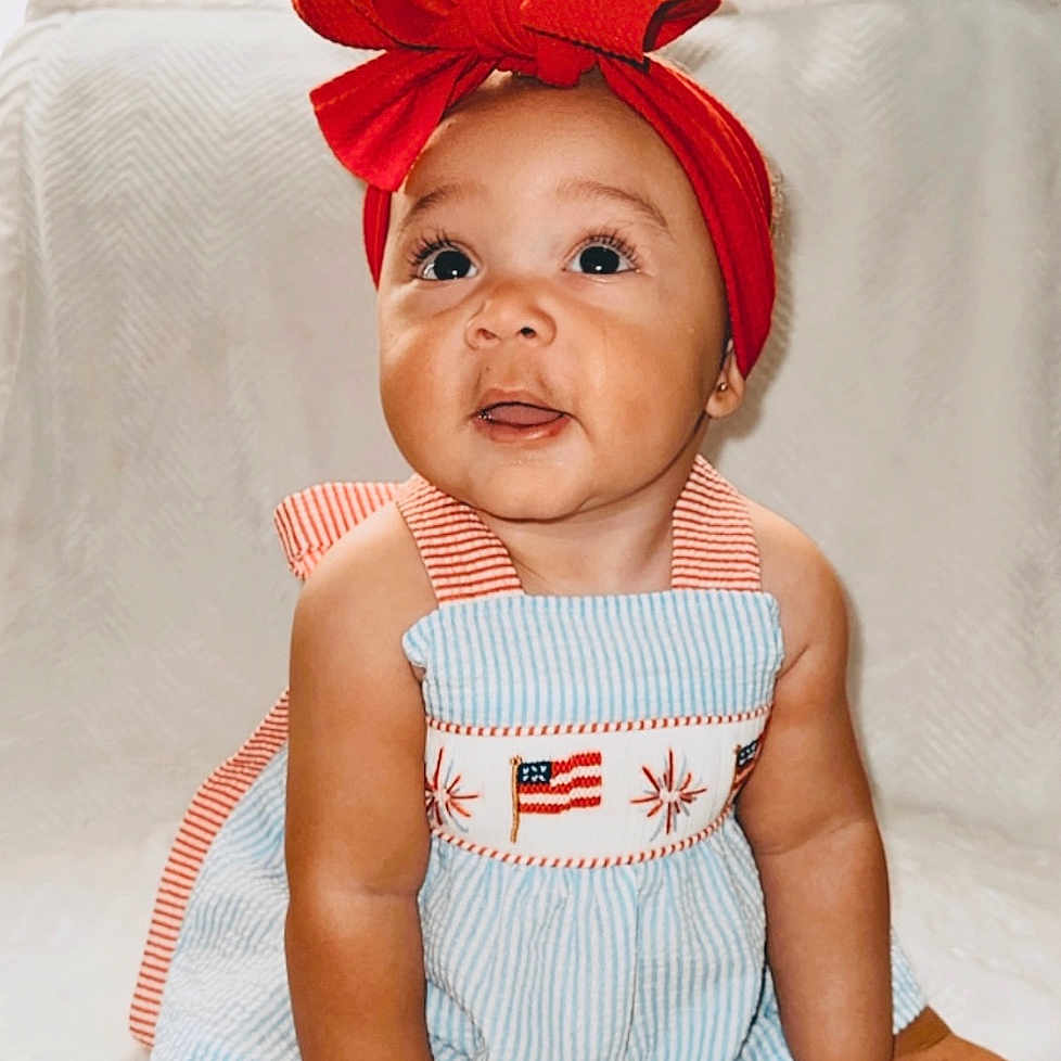 Kenzie is registered to the contest to win money with this photo: accessories, baby, babylaughing, bodypart, cap, clothing, couch, dress, face, finger, furniture, hand, happy, hat, head, person, photography, portrait, sitting, smile