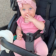Mia participe au concours pour gagner de l'argent avec cette photo : baby, child, stroller, pink_clothing, headband, blue_eyes, sitting, outdoor, footwearless, cute, infant, safety_harness, hand_on_face, toy, black_stroller, expression, person, portrait, playful, relaxed