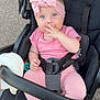 baby, child, stroller, pink_clothing, headband, blue_eyes, sitting, outdoor, footwearless, cute, infant, safety_harness, hand_on_face, toy, black_stroller, expression, person, portrait, playful, relaxed