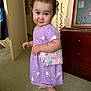 toddler, child, purple_dress, bunny_print, purse, barefoot, carpet, curly_hair, smile, indoor, dresser, furniture, wall_decor, toy, cute, person, standing, young_child, chubby_cheeks, playful
