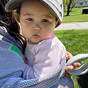 Sutton is registered to the contest to win money with this photo: baby, child, cap, hat, outdoor, grass, person, infant, holding, mesh_fabric, greenery, sunlight, face, expression, casual_wear, nature, daylight, portrait, cute, young