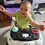 baby, walker, green_shirt, drool, happy, child, indoor, toy, floor, furniture, electronics, purple_cushion, smiling, person, head, arms, eyes, mouth, seat, home