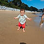 toddler, child, beach, sand, barefoot, sunny, trees, sky, clouds, beach_huts, water, shore, summer, vacation, outdoor, nature, person, clothing, shorts, shirt