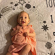 Esme joined the competition — help win amazing prizes! baby, infant, child, smiling, happy, portrait, lying_down, blanket, bed, dress, orange_clothing, crossed_legs, barefoot, face, eyes, open_mouth, indoor, warm_lighting, star_pattern, photography