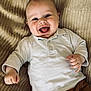 baby, blanket, brown_pants, casual, child, clothing, cute, face, hand, happy, indoors, infant, lying_down, person, portrait, skin, smiling, texture, white_shirt, young