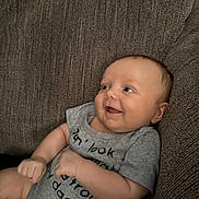 Bellamy is registered to the contest to win money with this photo: baby, infant, smile, couch, gray_onesie, happy, face, arm, hand, skin, textile, home, relaxation, seated, cute, child, indoors, portrait, person, cozy