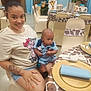 woman, baby, child, smile, tattoo, nails, shorts, tshirt, table, chair, balloons, party, giraffe_theme, table_setting, napkin, plate, indoor, decorations, plants, event