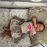 Jamilah is registered to the contest to win money with this photo: baby, crib, pillow, sheet, smile, child, infant, clothing, pattern, zebra_stripe, floral, cute, happy, lying_down, indoor, playful, person, small_child, toddler, resting