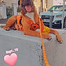brown_dog, cars, date_overlay, daylight, dog, happy, heart_sticker, large_dog, leash, lying_down, open_mouth, orange_harness, outdoor, residential_buildings, sidewalk, sitting, street, tongue_out, urban, yellow_toy